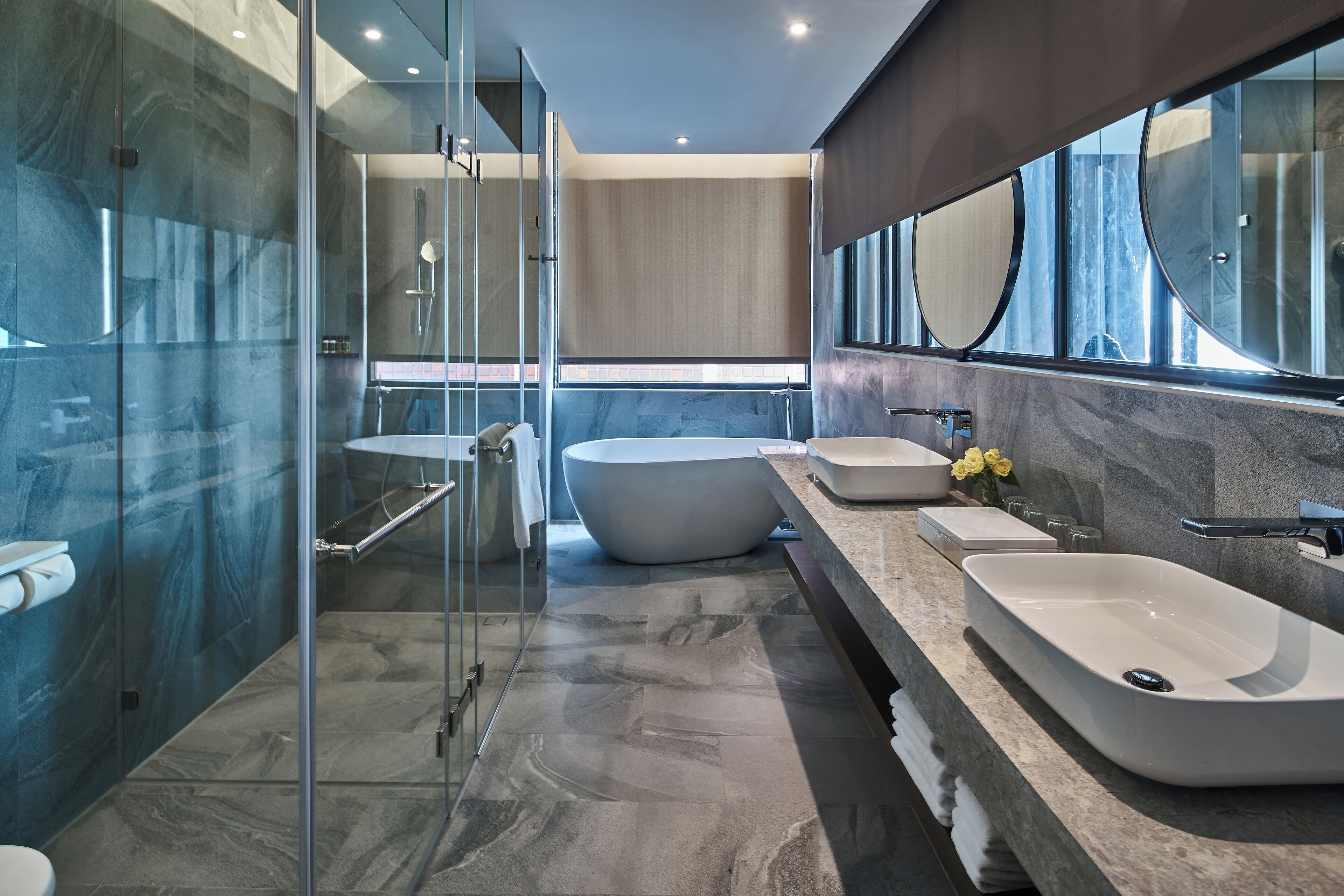 A modern bathroom with a glass-enclosed shower, a freestanding bathtub, and a large vanity with two sinks.
