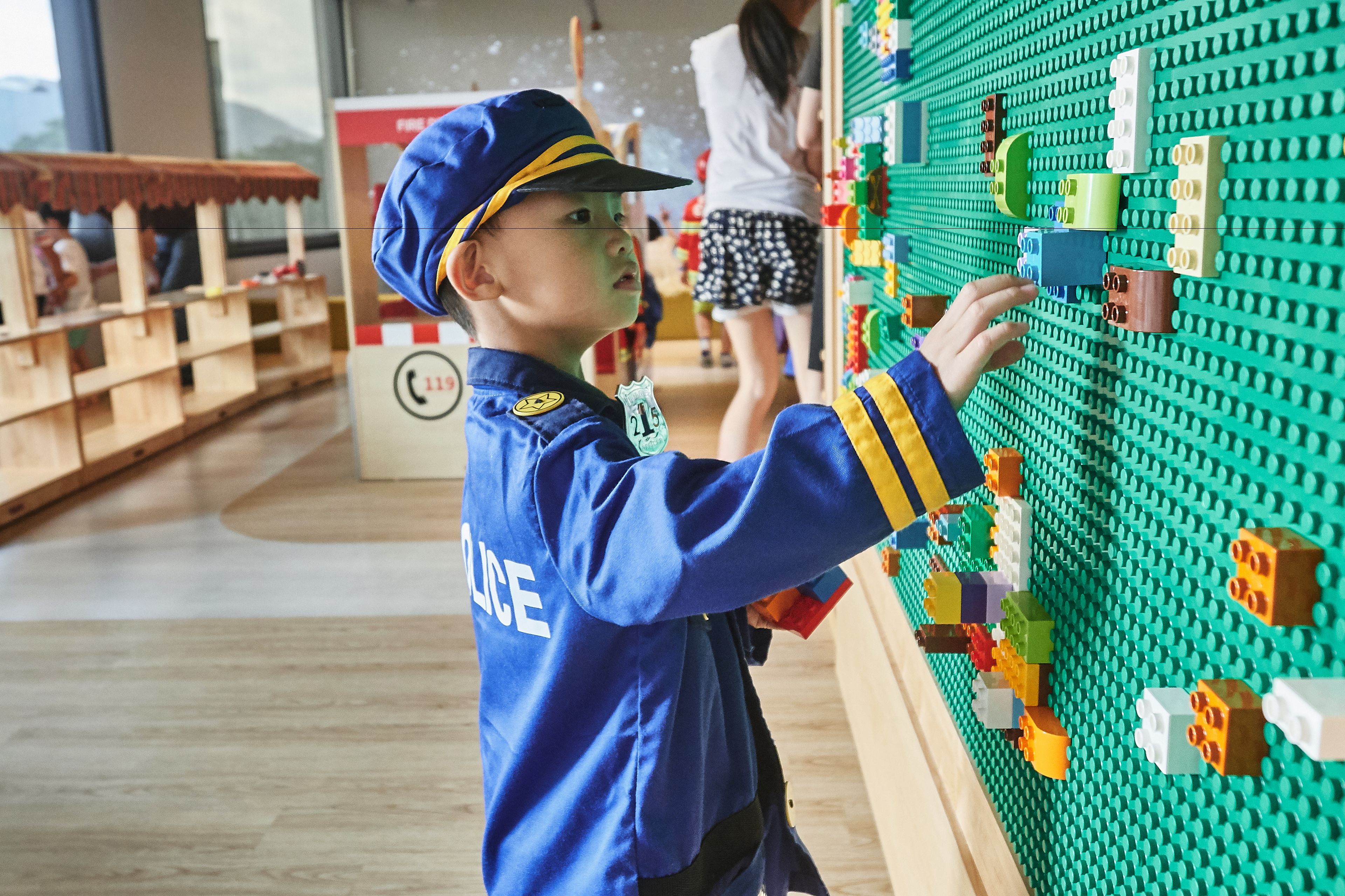 Ett barn i en blå uniform som leker med en vägg av LEGO-klossar.