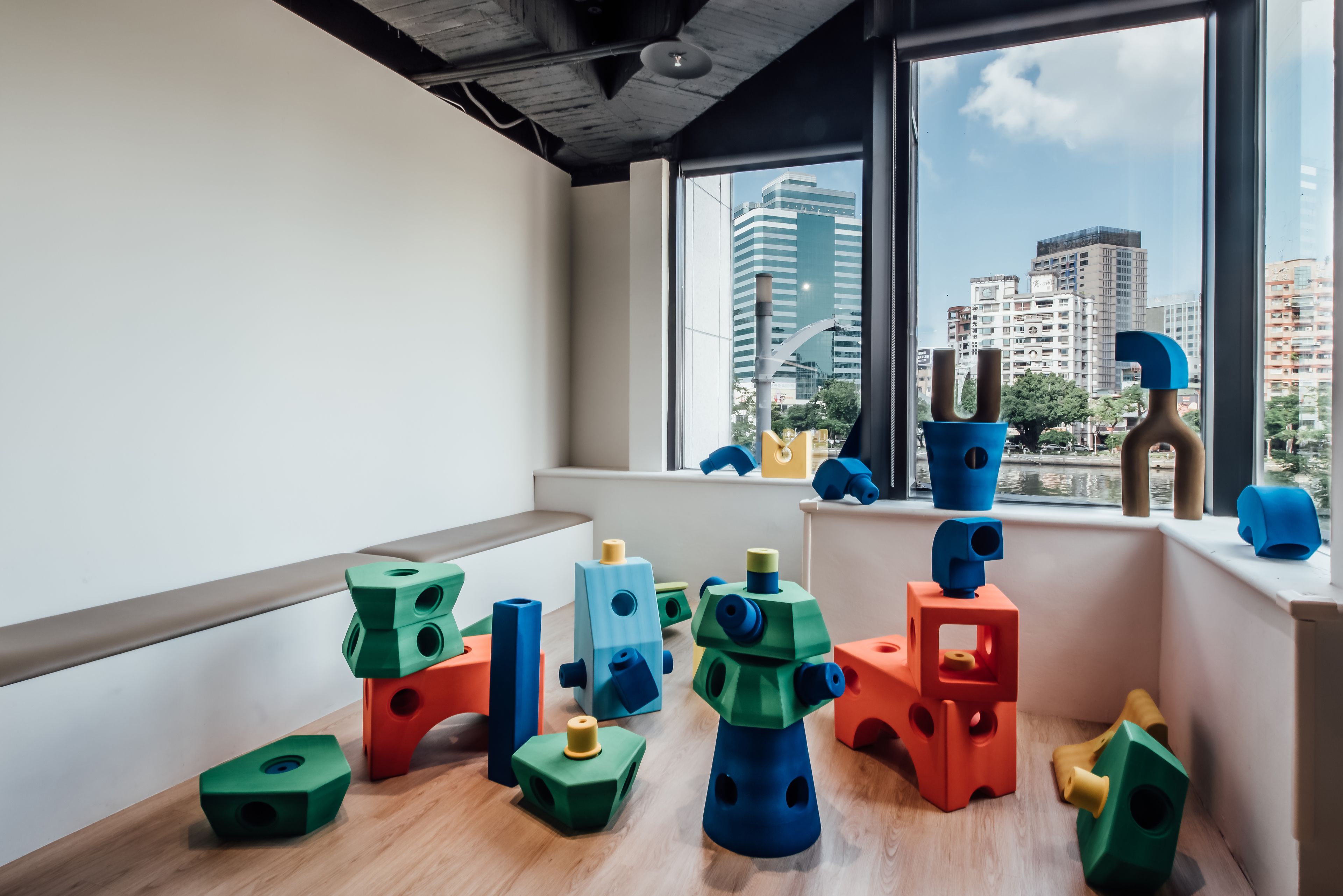 A room with a large window overlooking a cityscape, featuring colorful geometric blocks on the windowsill.
