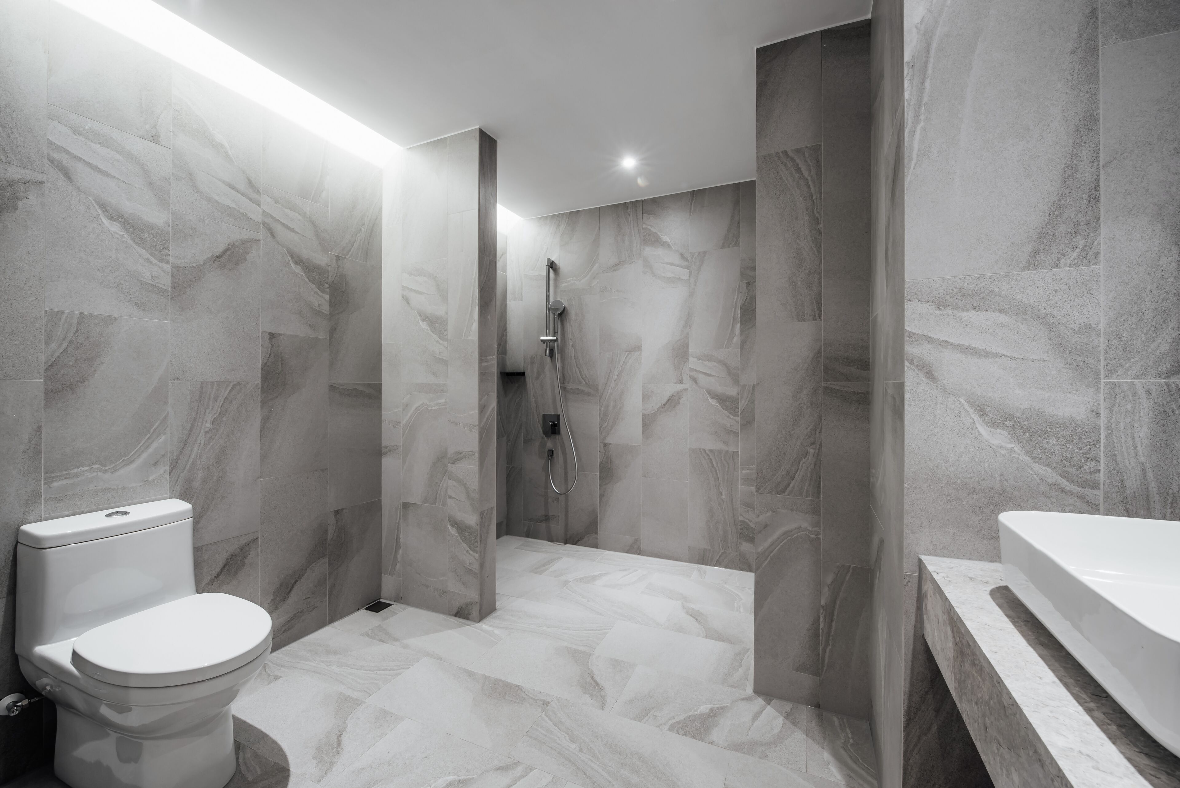 A modern bathroom with a toilet, shower, and bathtub, all with marble-like flooring and walls.