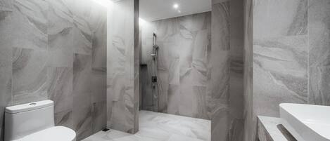 A modern bathroom with a toilet, shower, and bathtub, all with marble-like flooring and walls.