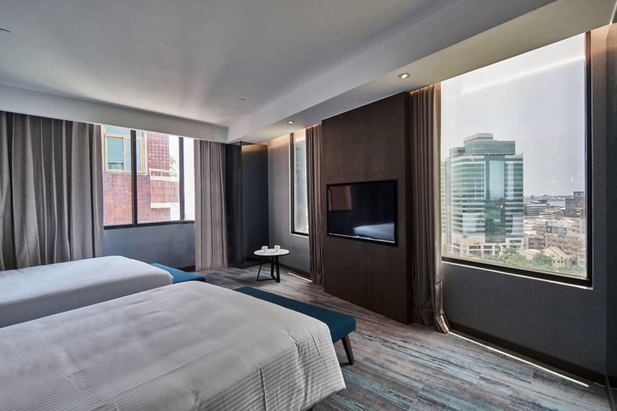 Habitación de hotel con dos camas, televisión, una mesita y vistas a la ciudad.