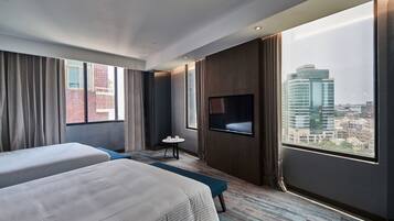 Ein Hotelzimmer mit zwei Betten, einem Fernseher, einem kleinen Tisch und Blick auf die Stadt.