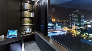 Habitación de hotel moderna con escritorio, laptop y ventana grande con vista a un paisaje urbano nocturno.
