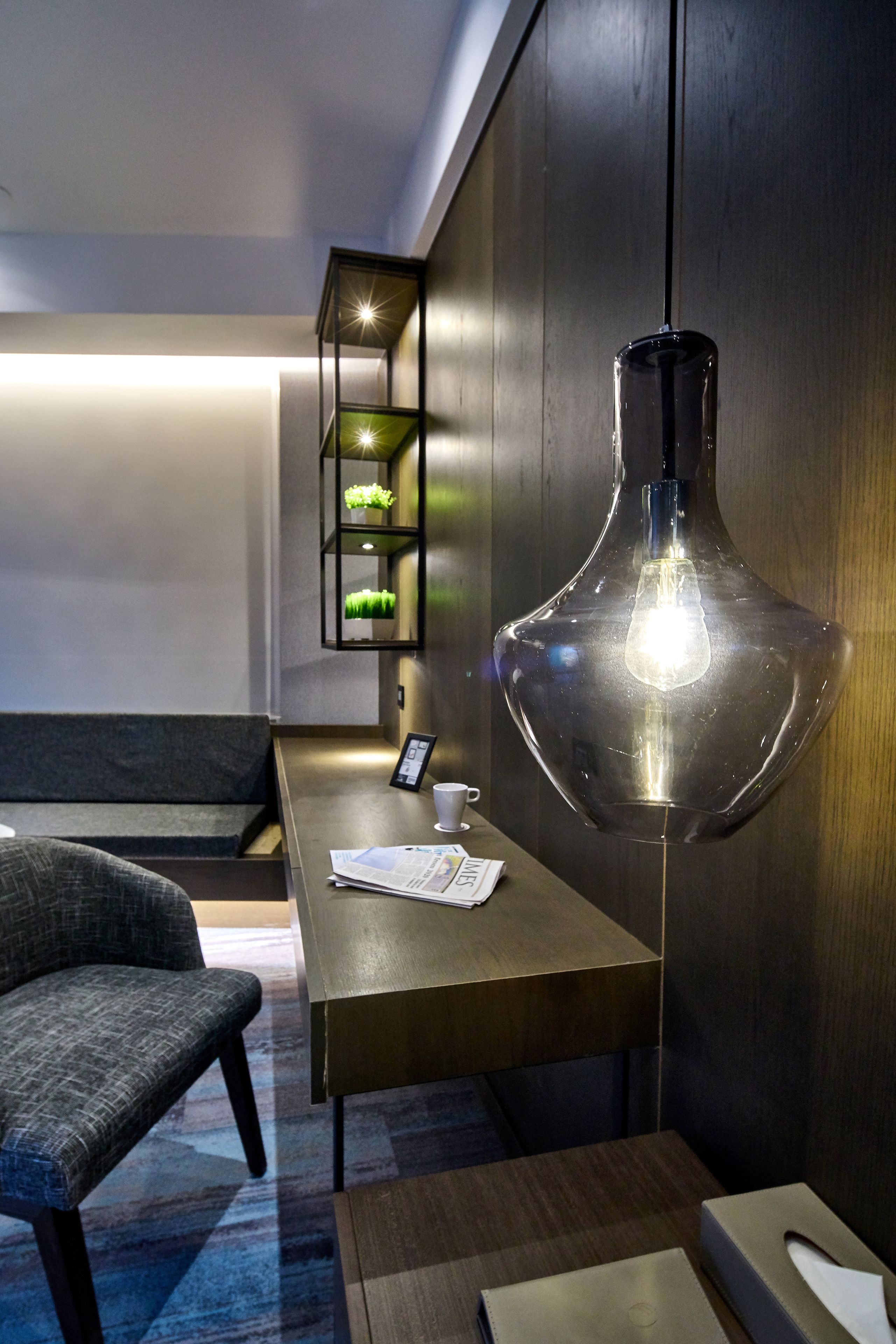 A modern room with a wooden desk, a chair, a unique pendant light, and a small shelf with greenery.
