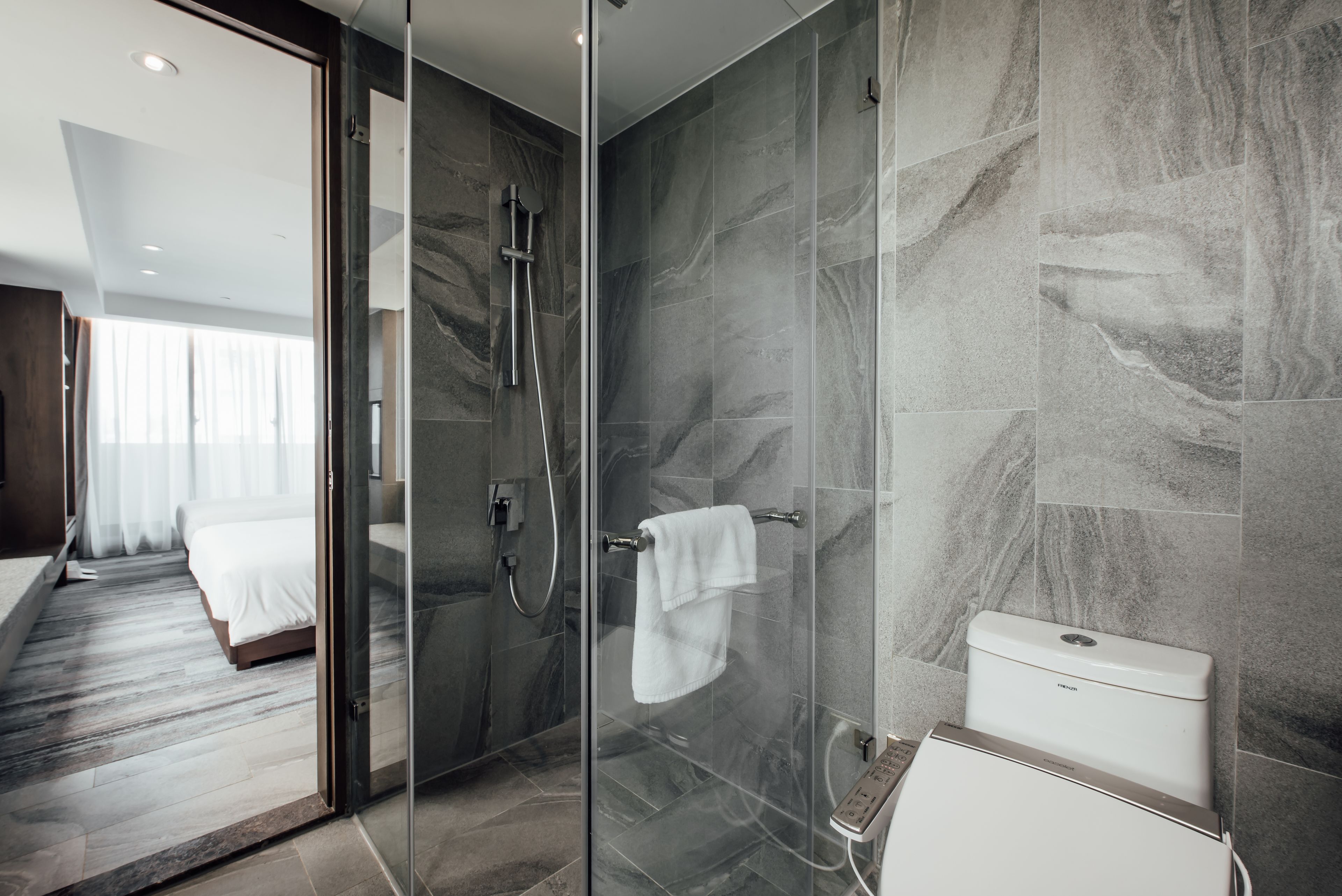 Un baño moderno con cabina de ducha de vidrio, inodoro y un perchero visible.