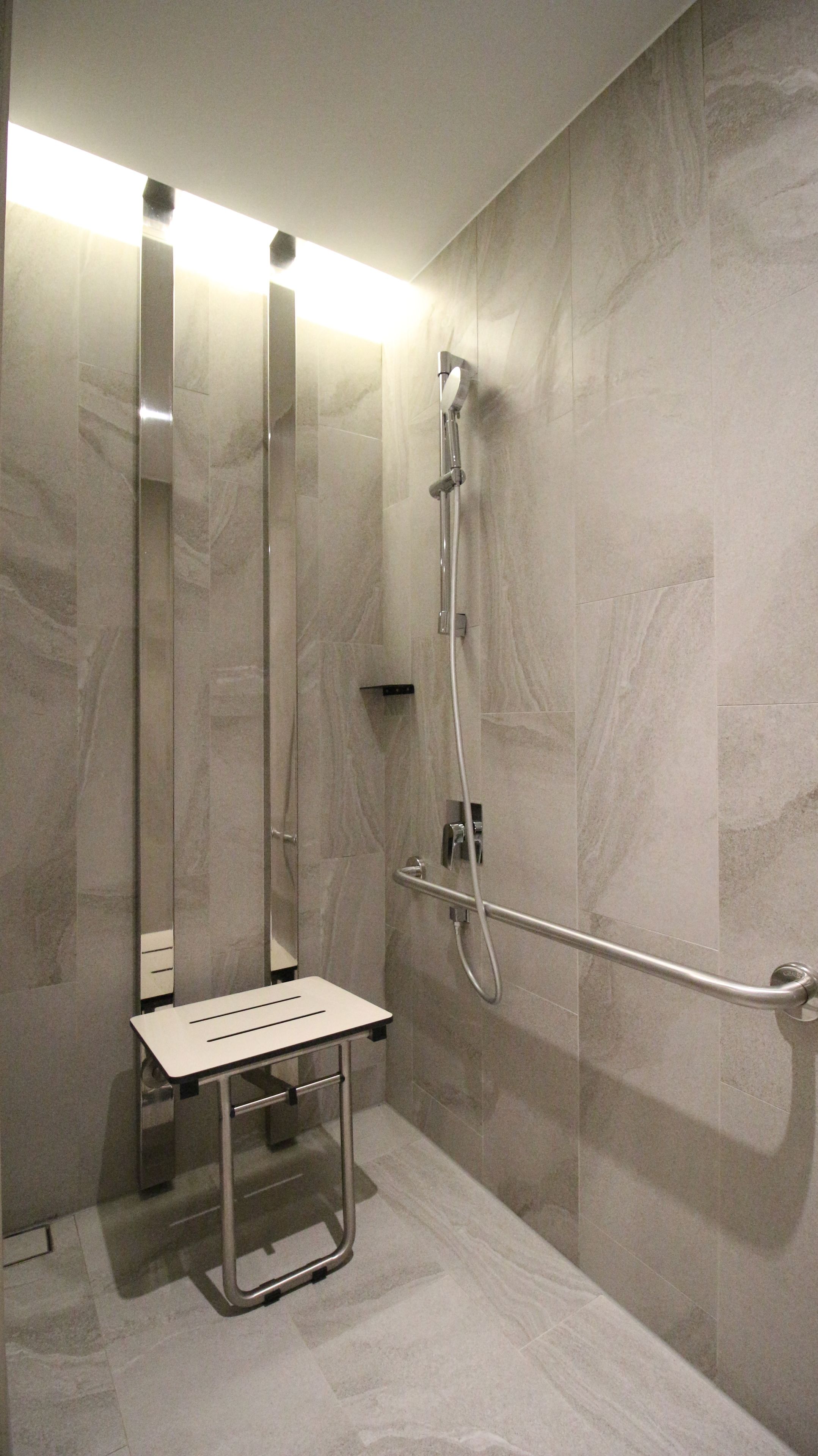 A modern bathroom with a walk-in shower, a grab bar, and a bench.