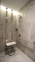 A modern bathroom with a walk-in shower, a grab bar, and a bench.