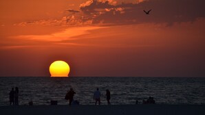 Atardecer sobre el océano con siluetas de personas en la playa.