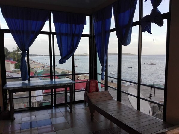 A room with a view of the sea, a wooden bench, and a table.