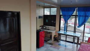 A compact room with a kitchenette, a bed, and a window with blue curtains. - Antipolo Beach Haus Annex (San Juan)