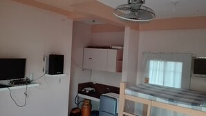 A small, compact room with a bunk bed, a television, a ceiling fan, and a kitchenette area. - Antipolo Beach Haus Annex (San Juan)