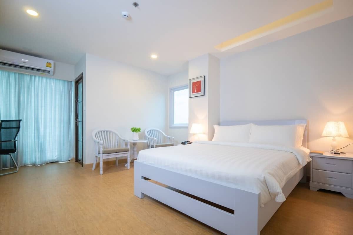 A modern hotel room with a large bed, a desk with a chair, and a small table with a plant.