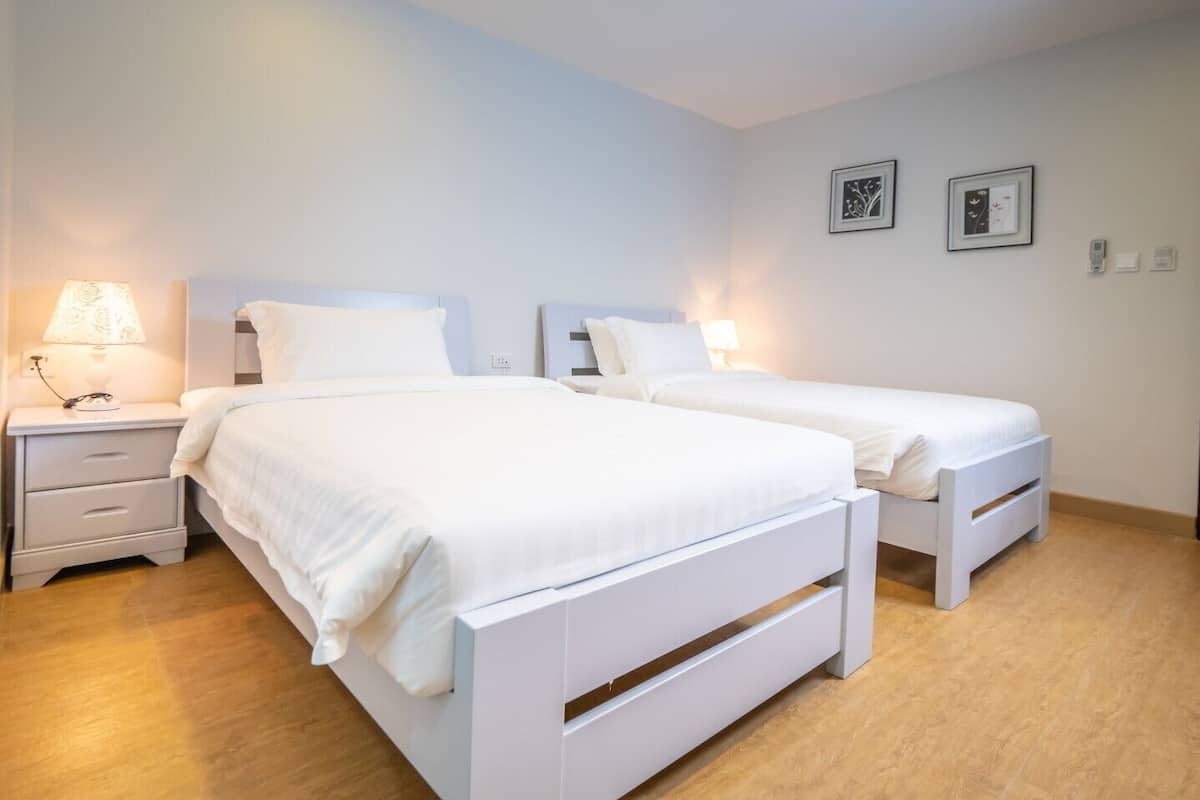 A hotel room with two single beds, a bedside table with a lamp, and a wall-mounted power outlet.