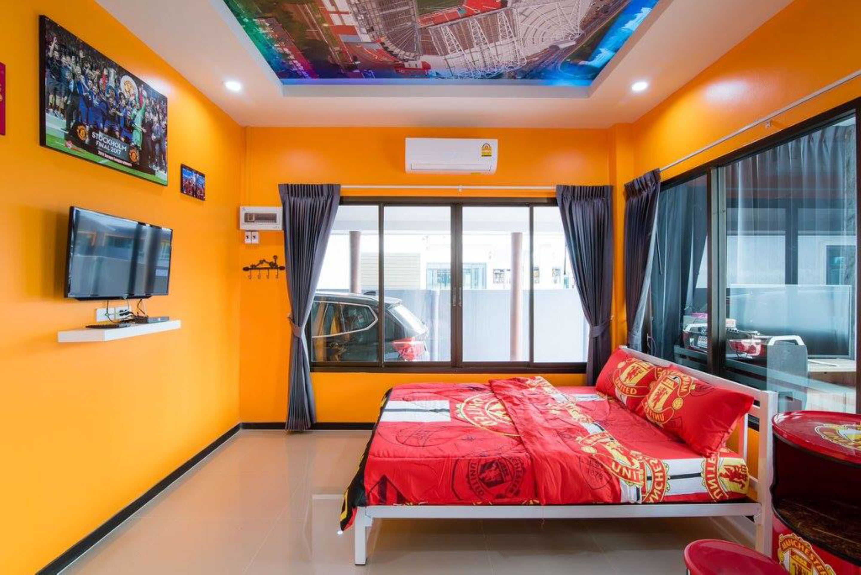 A hotel room with a bed, a television, a window with curtains, and a ceiling with a light fixture.