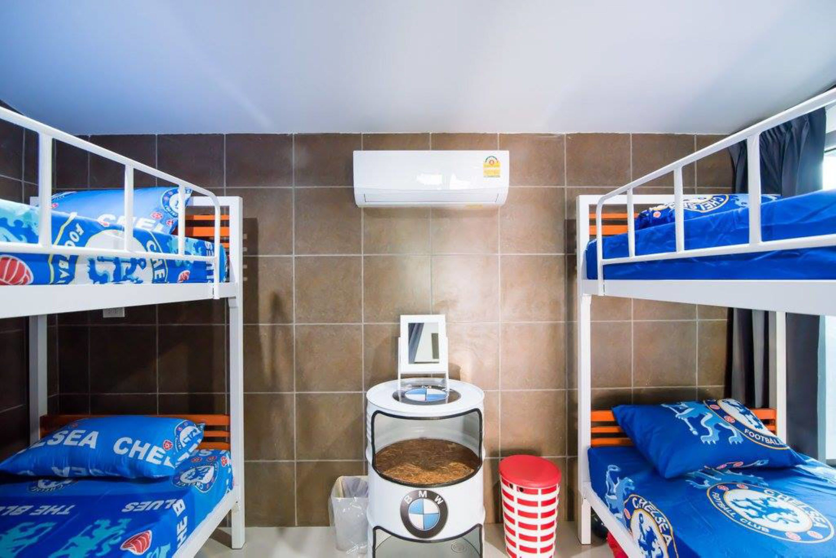 A room with two bunk beds, each with blue bedding featuring a football club logo, a small table with a coffee machine, and a window with curtains.