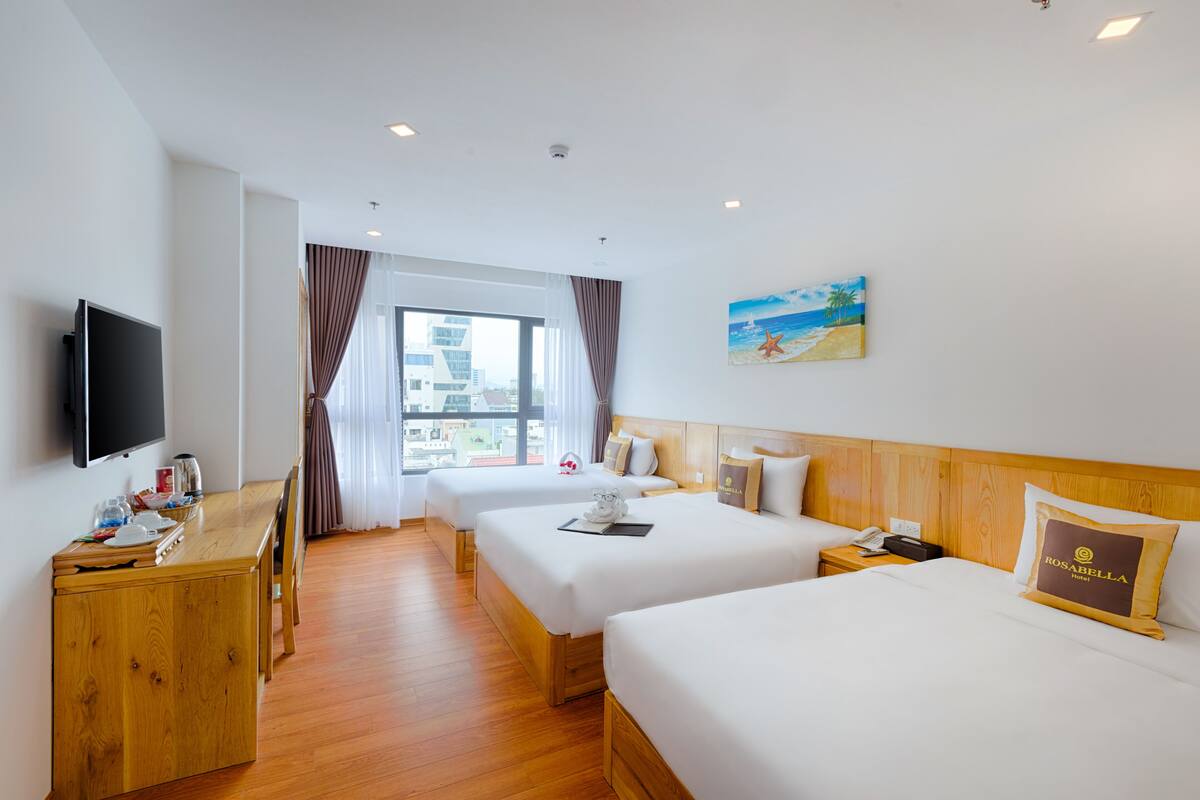 Ein Hotelzimmer mit zwei Betten, einem Fernseher, einem Holztisch und einem Fenster mit Vorhängen.