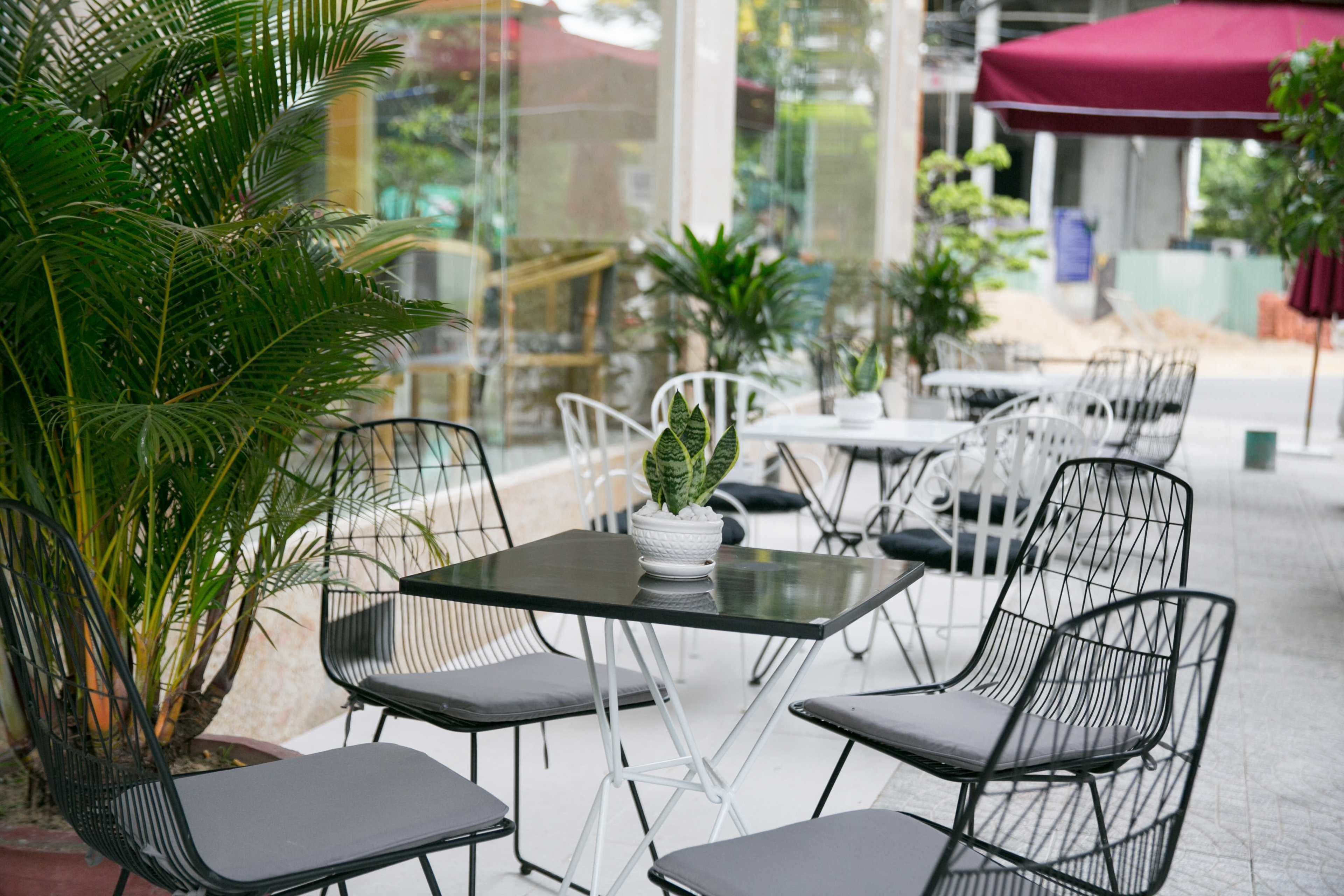Een terras met metalen stoelen en tafels, omgeven door plantenpotten.