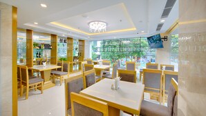 Un restaurant doté de nombreuses tables et chaises, d’un lustre et d’une grande fenêtre donnant sur l’extérieur.