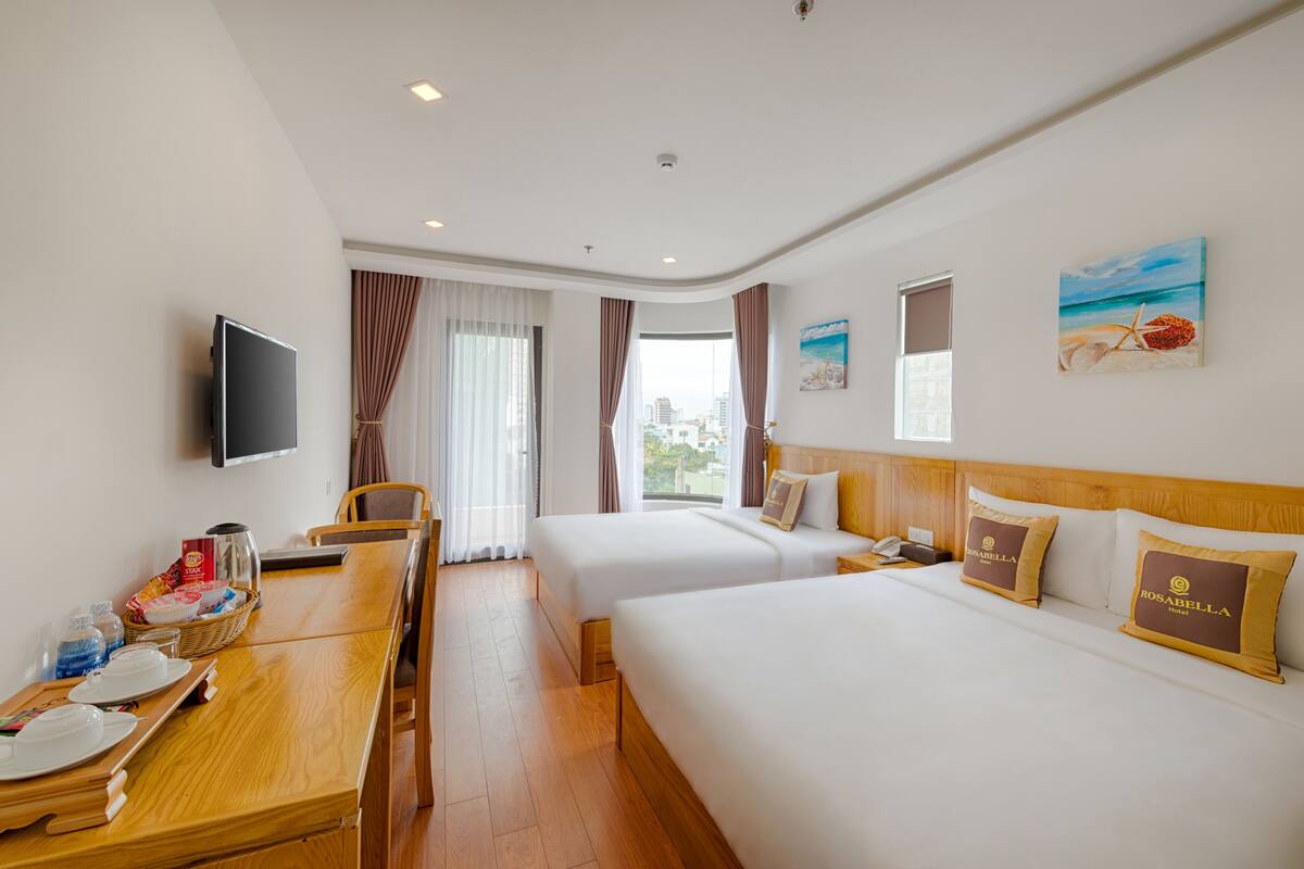 Ein Hotelzimmer mit zwei Betten, einem Fernseher, einem Esstisch mit Frühstücksangeboten und einem Fenster mit Vorhängen.
