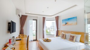 Une chambre d’hôtel comprenant un lit, un bureau avec une chaise, une télévision et une fenêtre avec des rideaux.