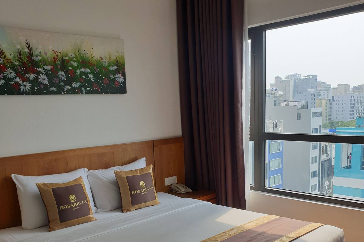 Ein Hotelzimmer mit einem großen Bett, Blick auf die Stadt und einem Gemälde an der Wand.
