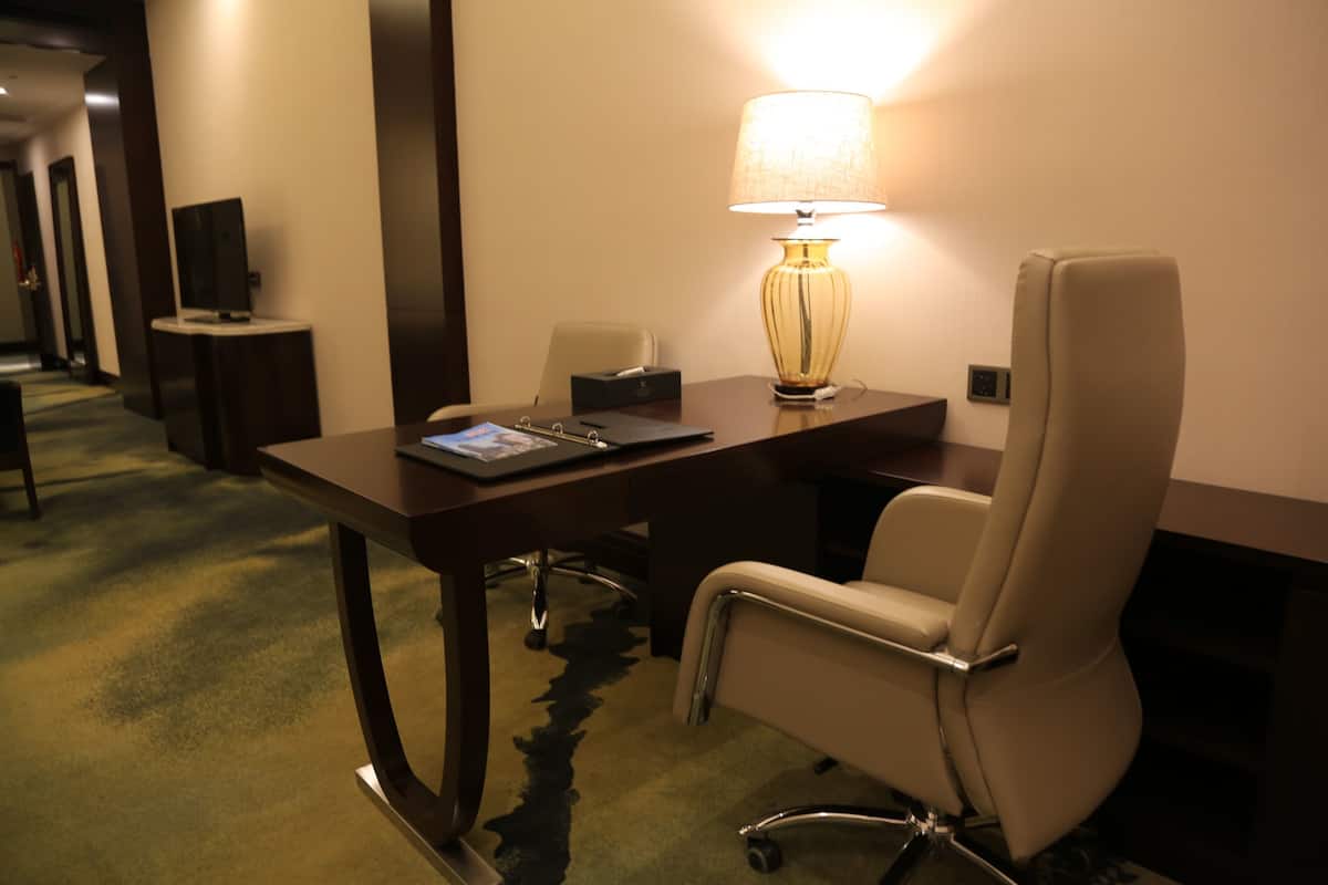 A hotel room with a desk, a chair, a lamp, and a television on a stand.