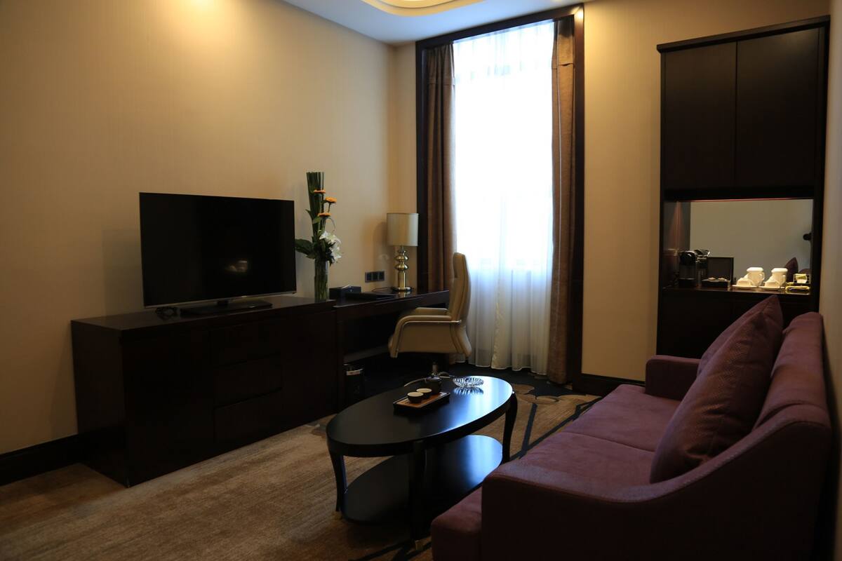 A modern hotel room with a flat-screen TV, a sofa, a coffee table, and a desk with a lamp.