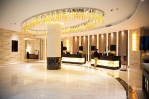 A spacious lobby with a marble floor, a central column, and a reception desk with a receptionist. - The Huiting Collection (Wuhan)