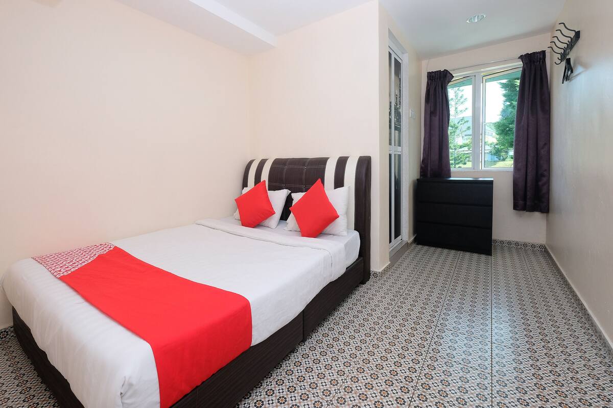 A hotel room with a bed, a window with curtains, a small black dresser, and patterned floor tiles.