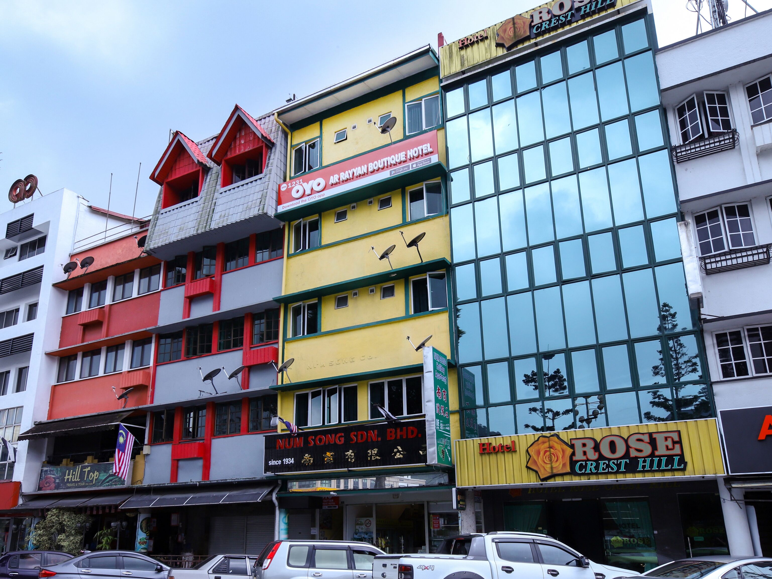 A multi-story hotel with a prominent yellow facade, a rooftop terrace, and a large glass window on the right side.