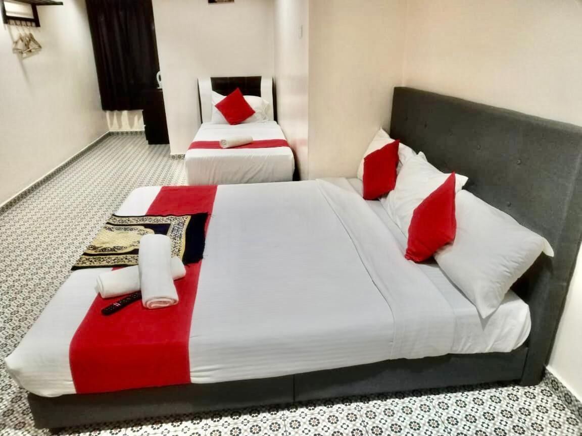 A hotel room with two beds, each with white bedding and red accents, a patterned floor, and a dark headboard.