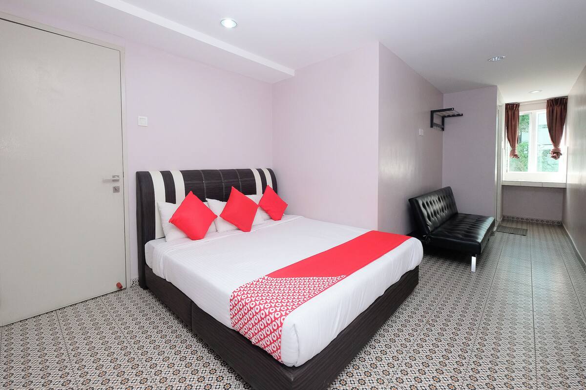 A hotel room with a bed, a chair, a window with curtains, and a door.