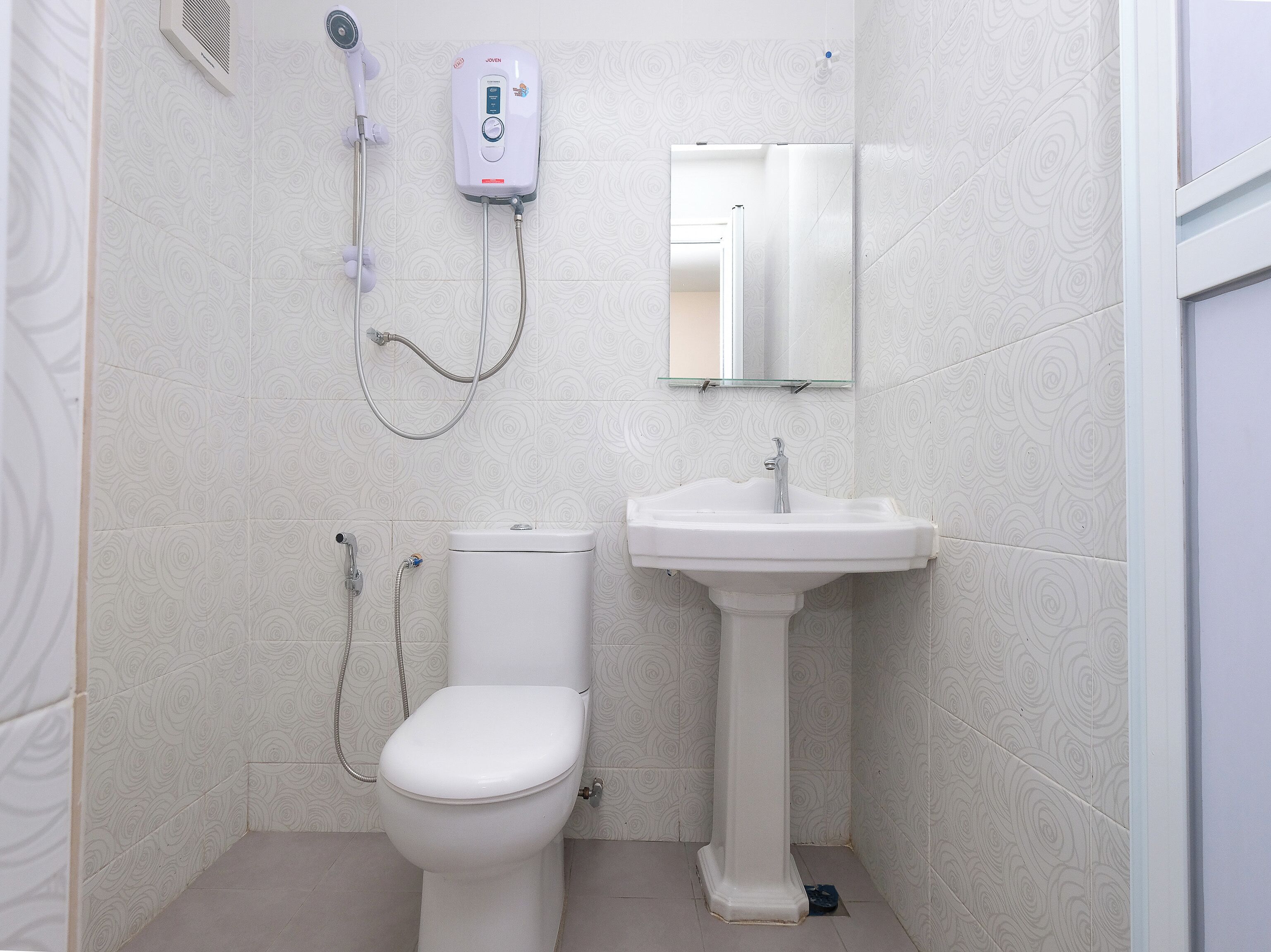 A bathroom with a toilet, a pedestal sink, and a handheld showerhead mounted on the wall.