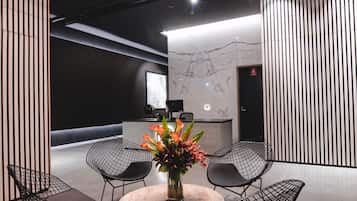 A modern reception area with a round table, four wireframe chairs, a vase with flowers, and a unique circular light fixture.