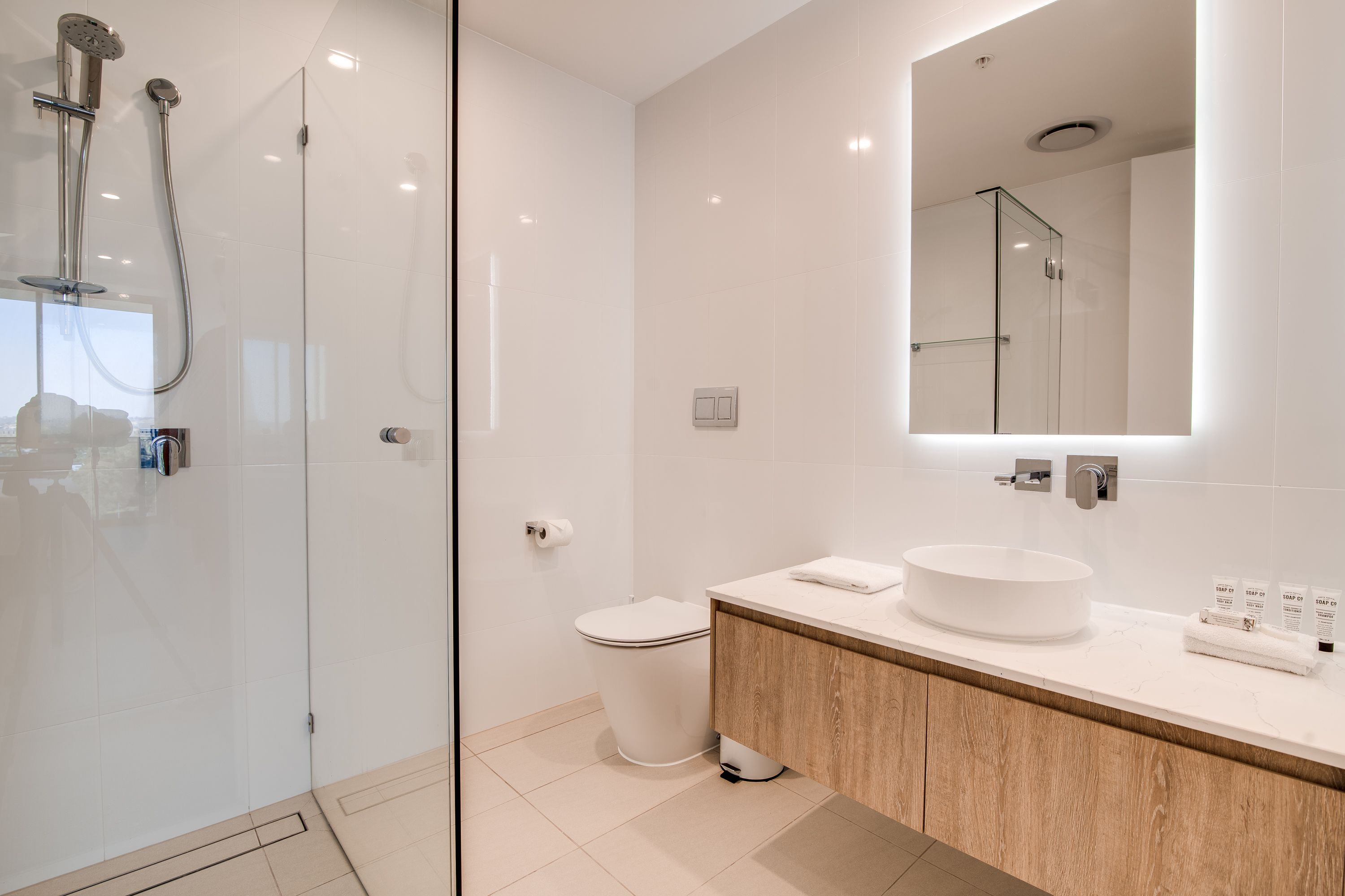 A modern bathroom with a glass-enclosed shower, a white toilet, and a wooden vanity with a round sink.
