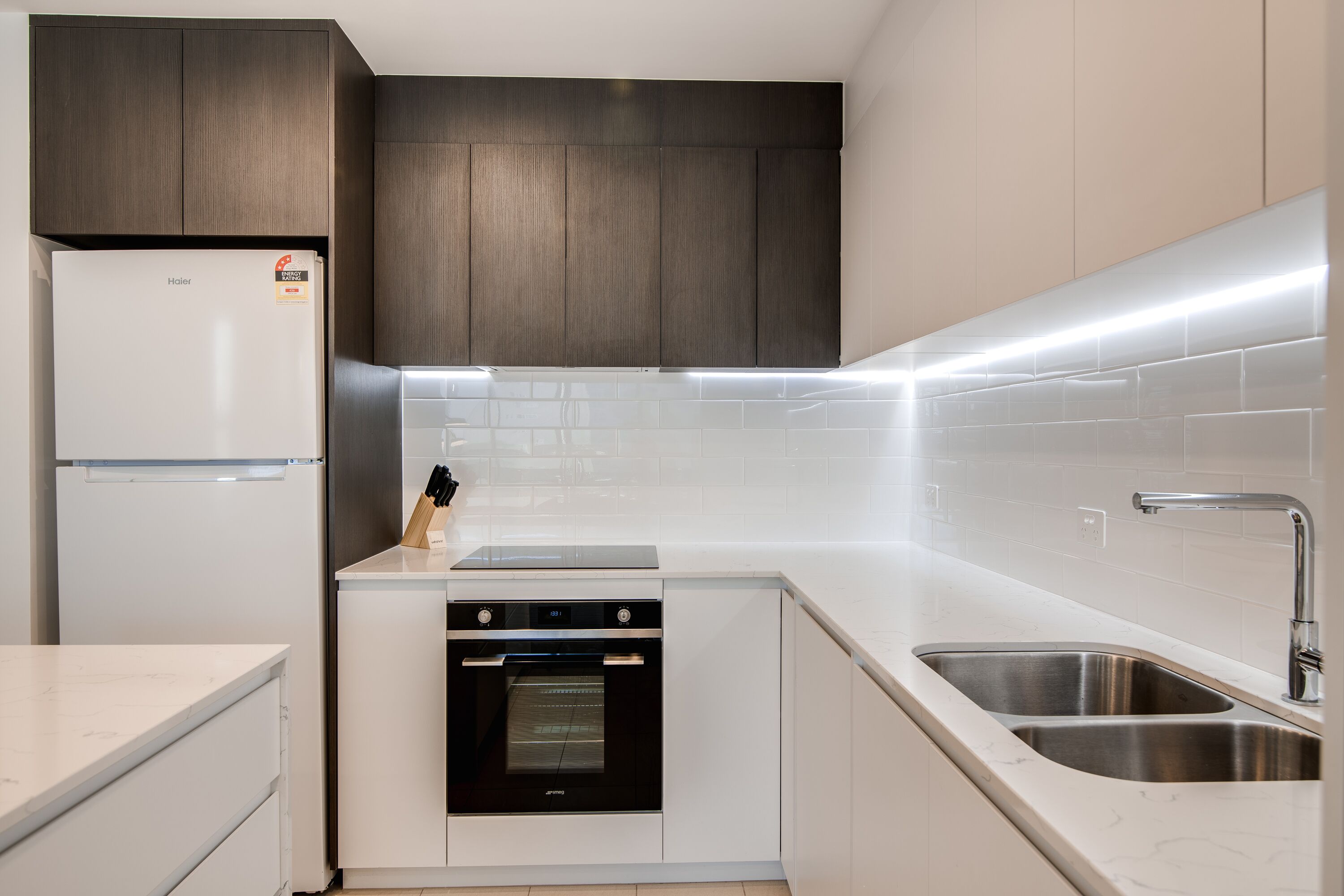 A modern kitchen with a built-in oven, a stainless steel sink, and a refrigerator.