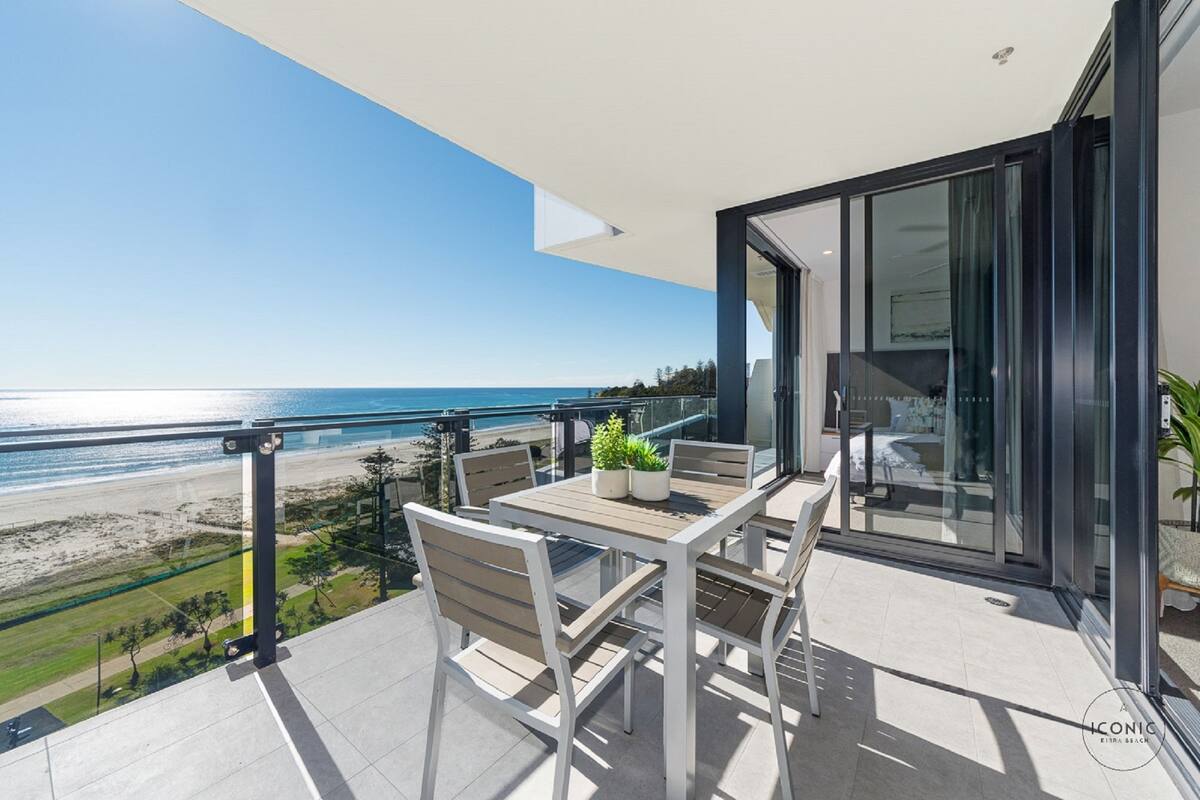 A balcony with a view of the beach, a table with chairs, and a glass door leading to an interior space.