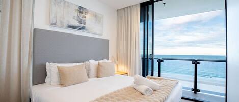 Ein modernes Hotelzimmer mit einem großen Bett, einem Deckenventilator, Blick auf den Ozean und einem Gemälde an der Wand.
