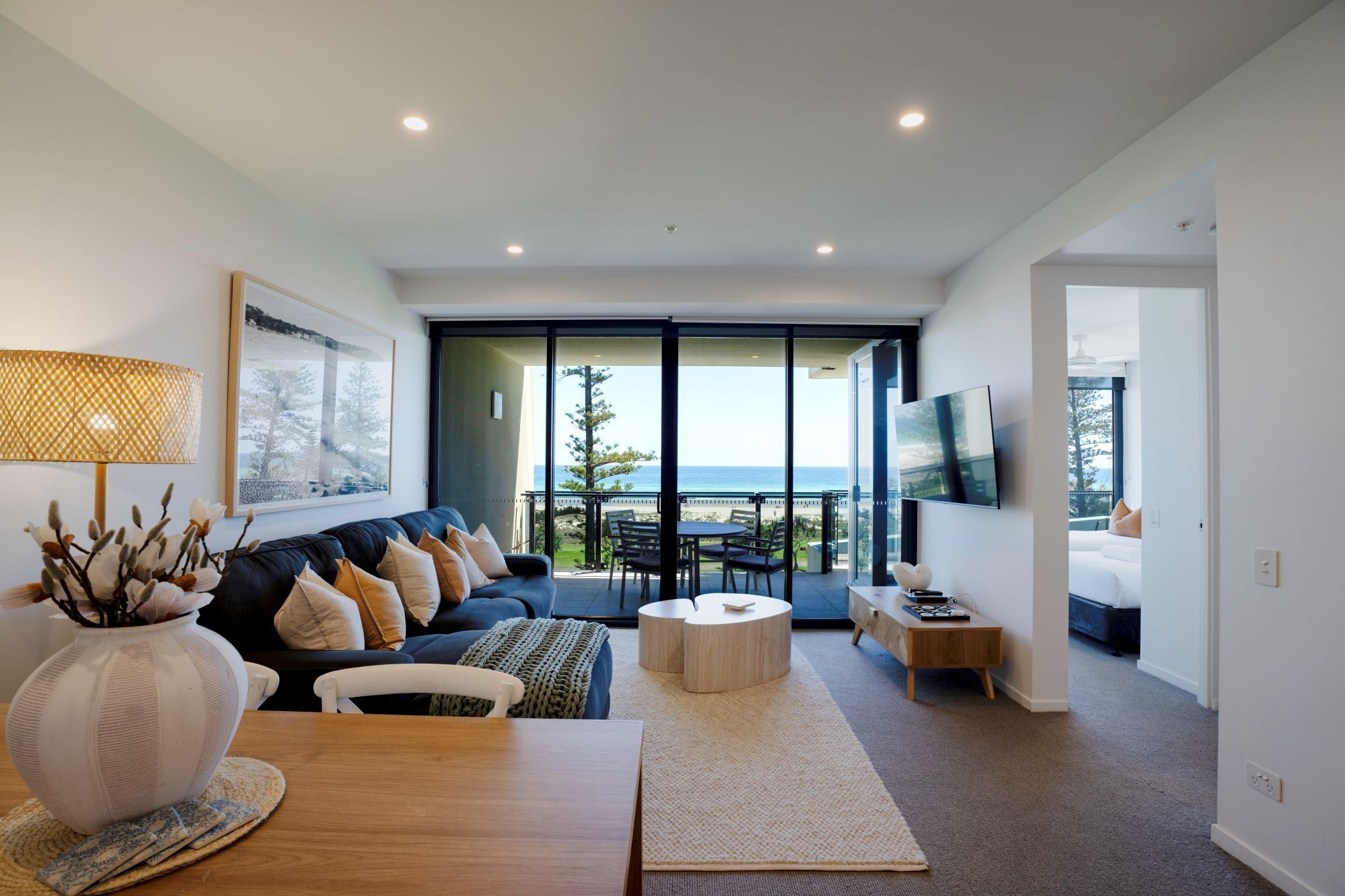 A modern living room with a sofa, coffee table, and a view of the ocean through large sliding doors.
