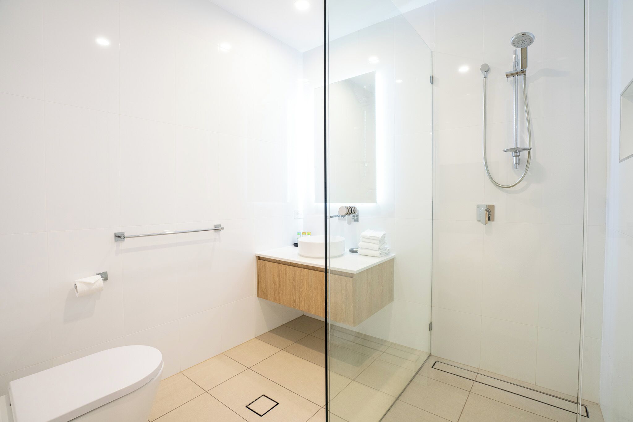 A modern bathroom with a glass shower enclosure, a white toilet, and a wooden vanity with a mirror.