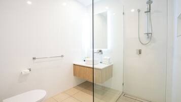 A modern bathroom with a glass shower enclosure, a white toilet, and a wooden vanity with a mirror.