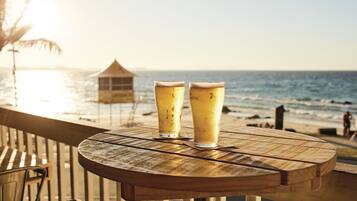 Una mesa de madera con dos vasos de cerveza en un balcón con vista al océano.