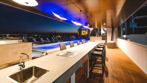 Zona de bar moderna con una barra larga, taburetes y una piscina al fondo.