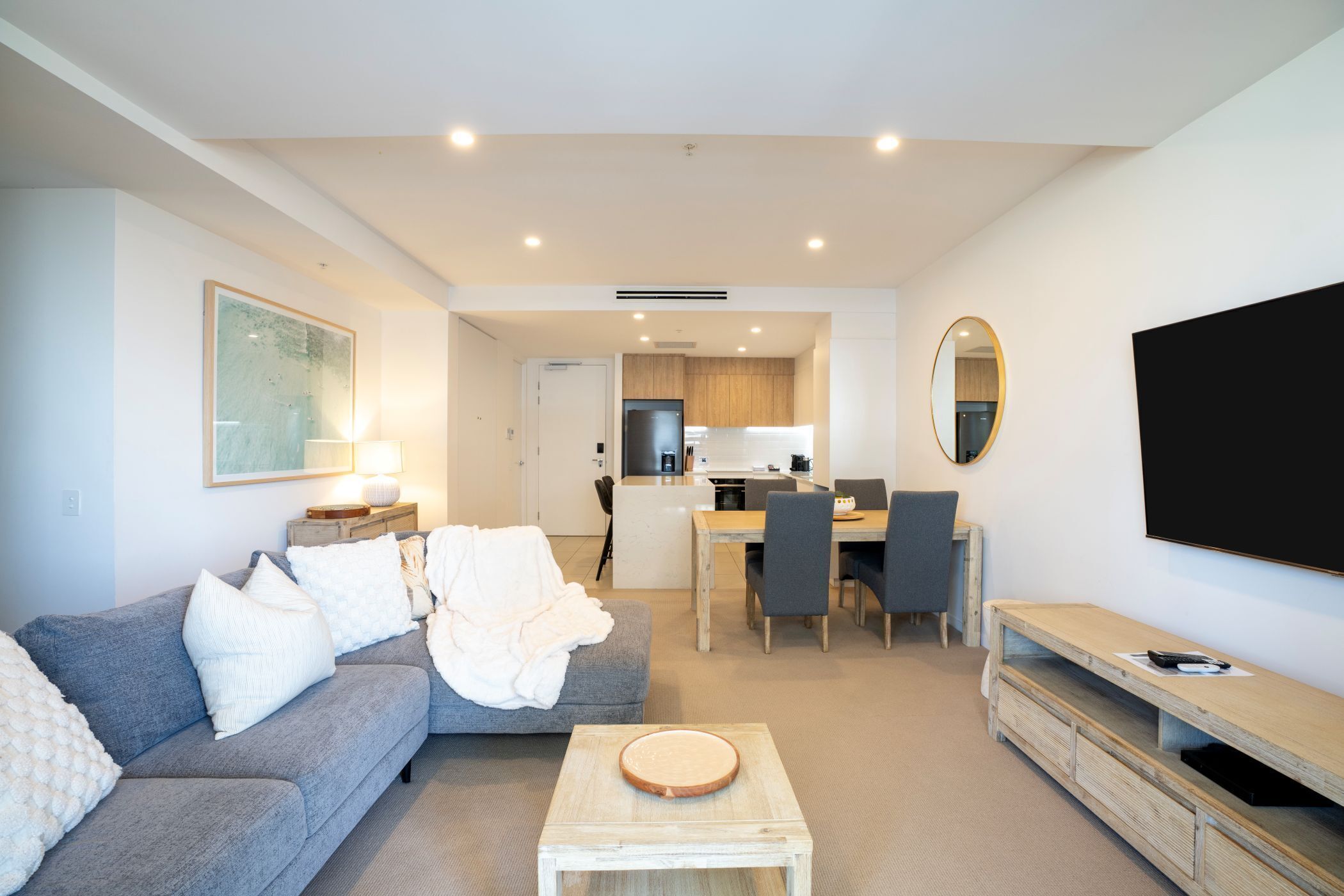 A modern living room with a grey sofa, a wooden coffee table, a TV stand, and a dining area with a table and chairs.