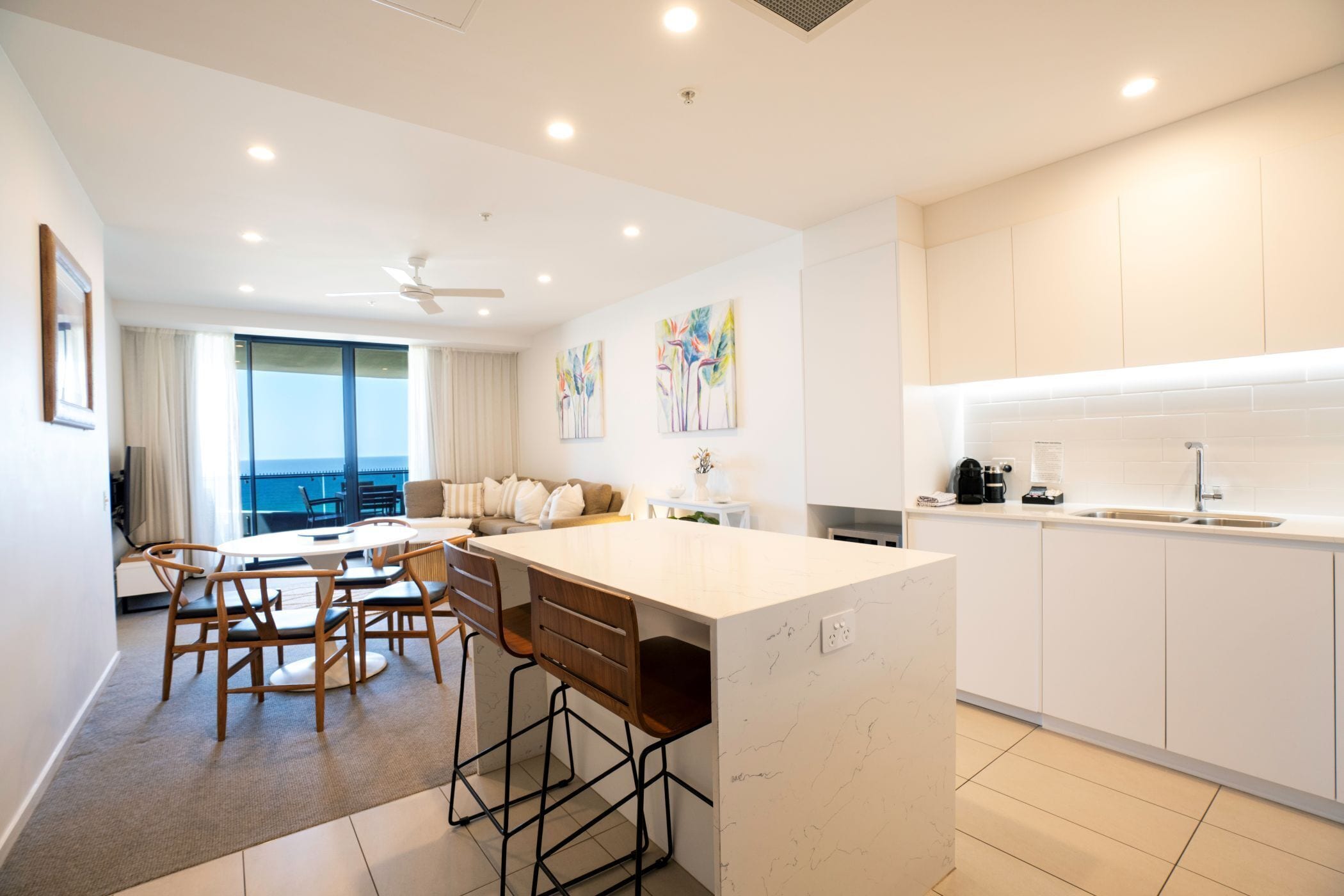 A modern kitchen with a central island, bar stools, and a dining area with a view.