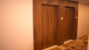 Un corridoio con due porte in legno, un tappeto decorato e un interruttore sulla parete.
