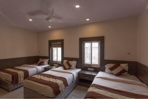 A hotel room with three single beds, a ceiling fan, and two windows with blinds. - Hari Vilaas (Varanasi)