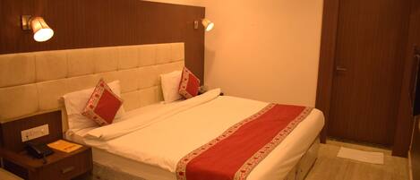 A hotel room with a large bed, a nightstand with a phone and a notepad, a wooden headboard, and a door with a towel rack.