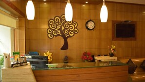 Una reception con un bancone di vetro, un orologio e un pannello decorativo a forma di parete alberata.
